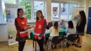 Dwie wolontariuszki Caritas stoją po lewej stronie zdjęcia. W tle widać stoisko WUP z pracownikiem, który obsługuje osoby siedzące przy biurku