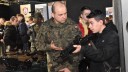 Po prawej stronie zdjęcia młody mężczyzna w czarnej bluzie trzyma w ręku broń automatyczną. Instruktor jednostki wojskowej przekazuję mu instrukcję. W tle widać młodzież zwiedzającą stoiska szkół oraz jednostek wojskowych na Forum Edukacyjnym w Ostrołęce.
